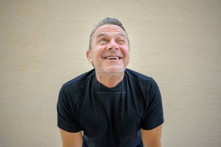 Foto de Alegre hombre de mediana edad inclinándose hacia delante hacia la cámara con una sonrisa divertida - Imagen libre de derechos