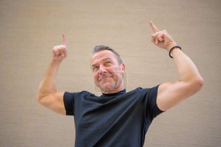 Photo for Attractive athletic middle aged man showing off his muscular upper arms while pointing fingers up - Royalty Free Image