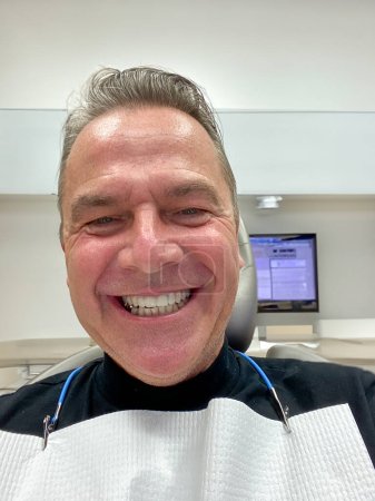 Photo for Close up front view of a man showing his new teeth with a bride smile at the dentist. - Royalty Free Image