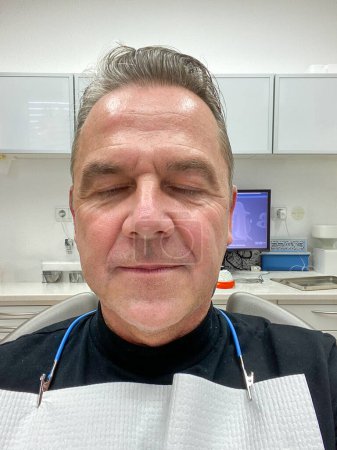 Téléchargez les photos : Vue de face d'un homme séduisant d'âge moyen avec les yeux fermés chez le dentiste. - en image libre de droit