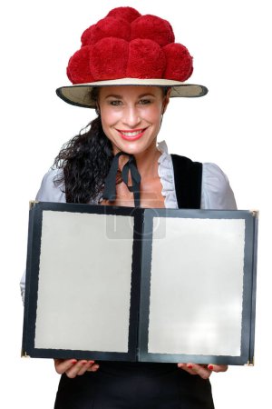 Pretty Black Forest waitress in a traditional Bollenhut with red pompoms holding open a blank menu with copy space with a friendly smile