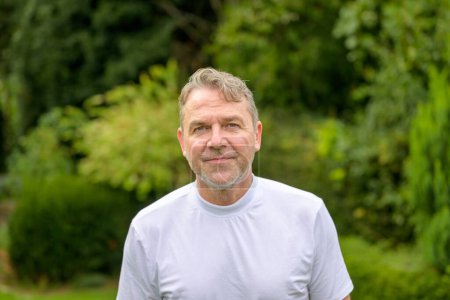Portrait of a serious and bitter middle-aged man looking at the camera while standing in the garden