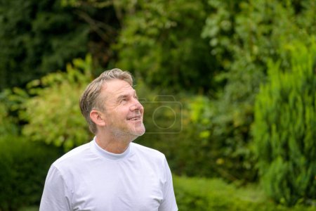 Foto de Hombre de mediana edad mira al cielo con una sonrisa alegre mientras está de pie en el jardín - Imagen libre de derechos