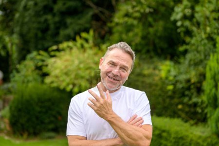 Foto de Atractivo hombre de mediana edad en sus 50 años sonriendo y haciendo un gesto de duda y cuestionabilidad mientras está de pie en el jardín - Imagen libre de derechos