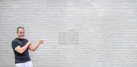 Téléchargez les photos : Photo promotionnelle d'un homme sympathique attirant pointant vers le côté droit devant un mur de briques blanches - en image libre de droit