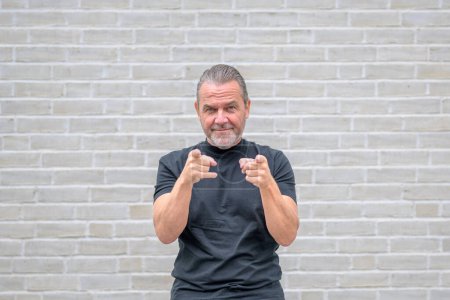 Photo for Portrait of an attractive friendly man pointing to the camera in front of a white brick wall - Royalty Free Image