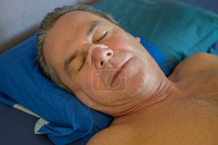 Nahaufnahme eines schlafenden Mannes mittleren Alters mit einem Nasenband im Bett liegend