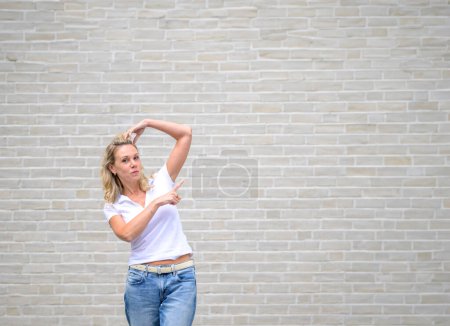 Foto de Foto promocional de una atractiva mujer amigable apuntando hacia el lado derecho frente a una pared de ladrillo blanco - Imagen libre de derechos