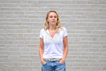 Photo for Upper body portrait of an attractive blonde woman looking at the camera with an arrogant look in front of a white brick wall - Royalty Free Image
