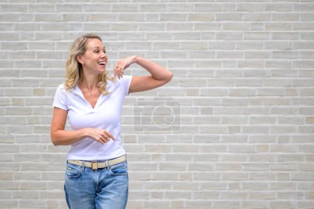 Foto de Retrato de la parte superior del cuerpo de una atractiva mujer amable mirando hacia un lado delante de una pared de ladrillo blanco - Imagen libre de derechos