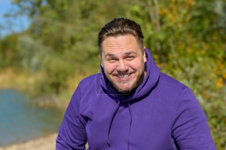 Photo for Portrait of a young attractive man wearing a purple hoodie laughing funny looking at the camera, outside in autumn - Royalty Free Image