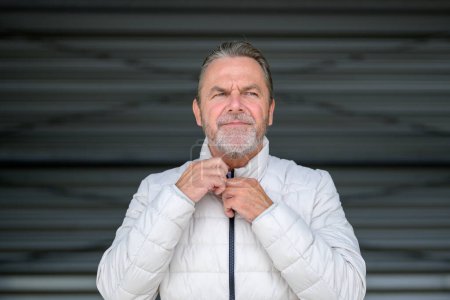 Photo for Portrait of a thoughtful attractive man in white winter jacket with his hands on the collar of the jacket looking to side - Royalty Free Image