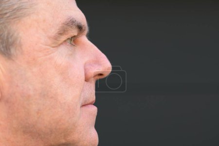Foto de Retrato extremo de vista lateral de un hombre de mediana edad con la boca cerrada sin prótesis dental frente a una pared negra - Imagen libre de derechos