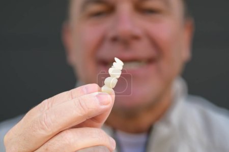 Foto de Extremo primer plano de un hombre sosteniendo su prótesis dental con los dedos, se centran en la mano - Imagen libre de derechos