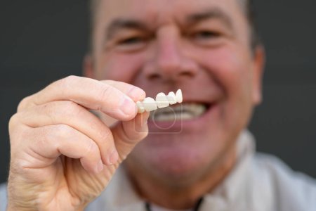 Photo for Extreme close up of a man holding his Dental prosthesis with his fingers, focus on hand - Royalty Free Image