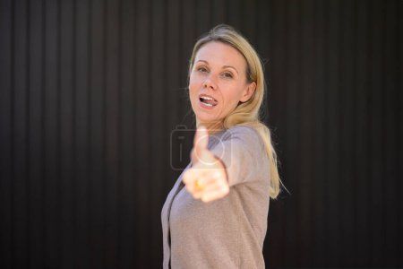 Photo for Side view of an attractive woman sticking out her tongue giving a thumbs up gesture, in front of wooden wall - Royalty Free Image