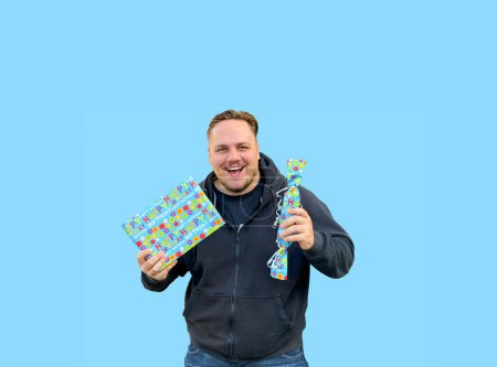 Téléchargez les photos : Heureux jeune homme tenant deux boîtes bleues avec espace de copie et regardant vers la caméra, dans le style de candycore - en image libre de droit