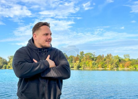 Téléchargez les photos : Jeune homme debout sur la rive du lac avec bras croisés en automne - en image libre de droit