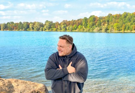 Photo for Close up of a young man standing on the bank of the lake with arm crossed in autumn - Royalty Free Image