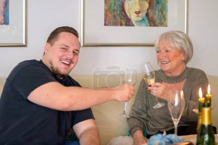 Téléchargez les photos : Le petit-enfant assis sur le canapé avec sa grand-mère et ils trinquent une belle fête avec du champagne - en image libre de droit