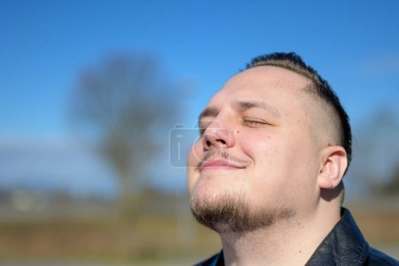Téléchargez les photos : Jeune homme séduisant profitant du soleil dans un parc avec les yeux fermés - en image libre de droit