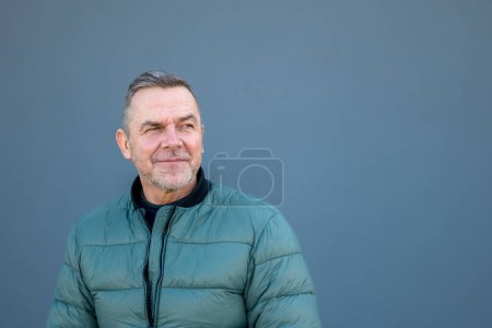 Foto de Retrato de la parte superior del cuerpo de un hombre de mediana edad mirando de lado a la distancia con una mirada crítica usando una chaqueta verde - Imagen libre de derechos
