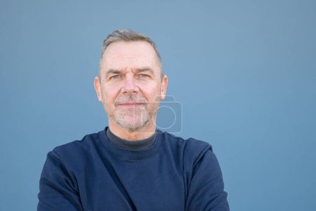 Foto de Retrato de cerca de un hombre de mediana edad mirando amigable a la cámara con un suéter azul - Imagen libre de derechos