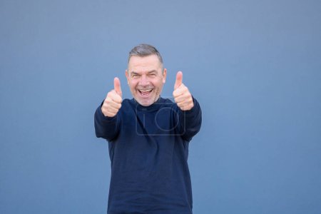 Téléchargez les photos : Enthousiaste motivé attrayant homme d'âge moyen donnant un double pouce geste d'approbation et de succès avec un sourire rayonnant - en image libre de droit