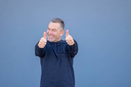 Téléchargez les photos : Enthousiaste motivé attrayant homme d'âge moyen donnant un double pouce geste d'approbation et de succès avec un sourire rayonnant - en image libre de droit