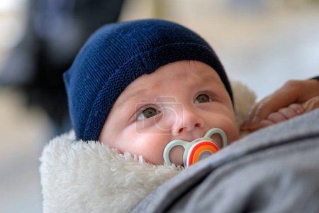 Téléchargez les photos : Extrême gros plan du petit bébé heureux avec de gros yeux levant les yeux avec une sucette et un chapeau bleu en plein air - en image libre de droit