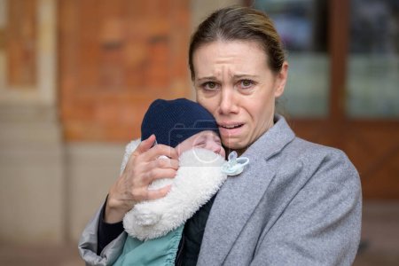 Porträt einer extrem erschöpften und gestressten Mutter in den Vierzigern, die ihr Neugeborenes hält und im Freien in die Kamera weint