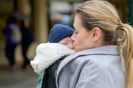 Téléchargez les photos : Belle blonde tardive mère dans la quarantaine tenant amoureusement son nouveau-né dans un porte-bébé et l'embrassant doucement sur le nez - en image libre de droit