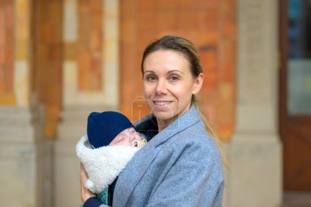 Téléchargez les photos : Portrait d'une mère à terme extrêmement heureuse dans la quarantaine tenant son nouveau-né et souriant à la caméra extérieure - en image libre de droit