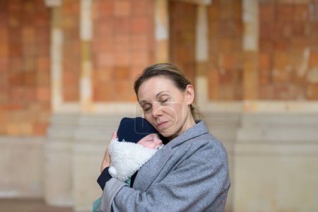 Photo for Happy late-term mother in her 40s holding her newborn baby and both with eyes closed outdoor - Royalty Free Image