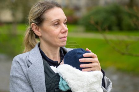 Téléchargez les photos : Gros plan d'une femme heureuse tenant et portant son bébé dans un porte-bébé dans un parc - en image libre de droit