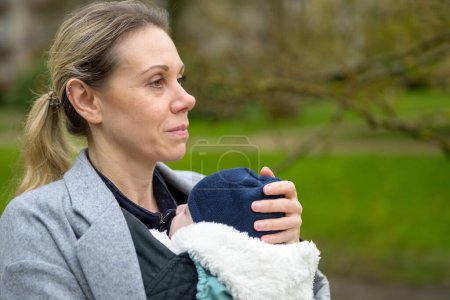 Téléchargez les photos : Gros plan d'une femme heureuse tenant et portant son bébé dans un porte-bébé dans un parc - en image libre de droit