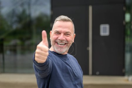 Téléchargez les photos : Enthousiaste motivé attrayant homme d'âge moyen donnant un pouce geste d'approbation et de succès avec un sourire rayonnant - en image libre de droit
