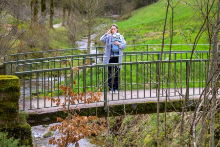 Téléchargez les photos : Femme stressée, épuisée et déprimée debout sur un pont dans la nature avec son petit bébé - en image libre de droit