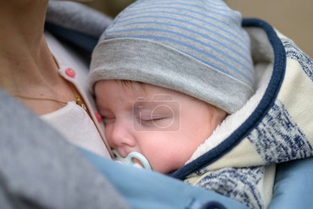 Téléchargez les photos : Extrême gros plan d'un bébé dormant dans un porte-bébé, dans une extraordinaire proximité de sa mère portant un chapeau rayé bleu et blanc - en image libre de droit