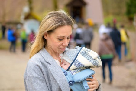 Téléchargez les photos : Portrait d'une femme heureuse regardant son bébé tout en le tenant et le portant dans un porte-bébé dans une ville - en image libre de droit