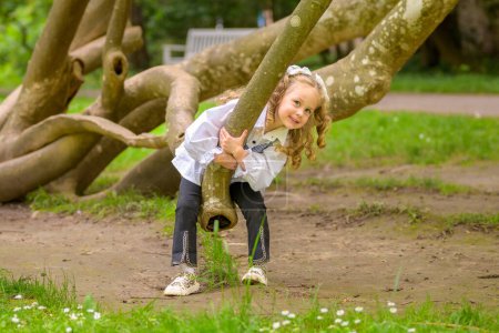 A playful young girl with curly hair is climbing a tree outdoors.