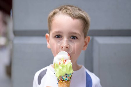 Un jeune garçon aux cheveux courts jouit d'un cône de crème glacée coloré recouvert d'aspersions.