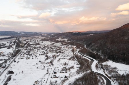 Téléchargez les photos : Aerial view of winter mountains, river and small town. Beautiful sunset with orange and blue clouds. - en image libre de droit