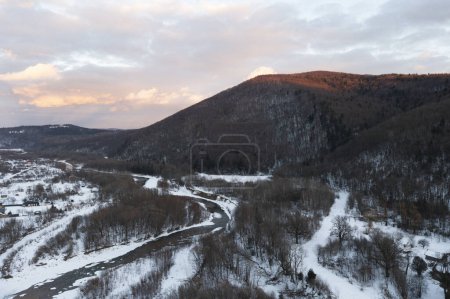 Téléchargez les photos : Aerial view of winter mountains, river and small town. Beautiful sunset with orange and blue clouds. - en image libre de droit