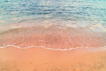 Heitere Strandszene mit sanften Wellen, die auf sandiges Ufer treffen. Blaues klares Wasser, oranger Sand. Kopieren Raum Sommerferien Anzeigen Hintergrund.