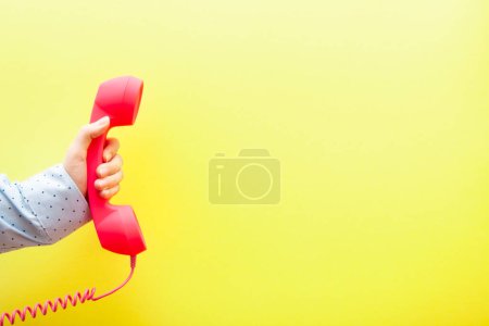 Foto de Mano de mujer con teléfono rosa sobre fondo amarillo con espacio de copia, comunicación y concepto de conexión - Imagen libre de derechos