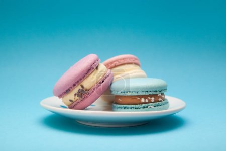 Foto de Pasteles de macarrones de diferentes colores en el plato sobre fondo azul, postre y comida dulce - Imagen libre de derechos