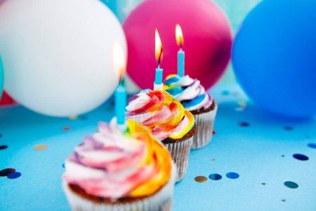 Foto de Tres cupcake con velas sobre fondo azul con globos de aire de colores, tarjeta de celebración - Imagen libre de derechos
