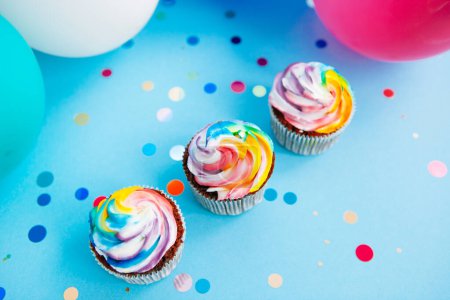Foto de Tres colores arco iris cupcake sobre fondo azul con globos de aire de vista superior - Imagen libre de derechos