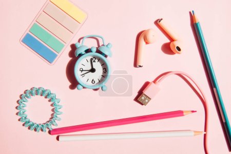 Foto de Reloj despertador azul y lápices, auriculares y artículos de papelería sobre fondo rosa, conjunto femenino como concepto de educación - Imagen libre de derechos